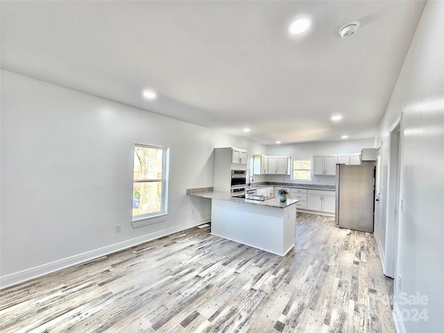 kitchen featuring kitchen peninsula, stainless steel fridge, stone countertops, light hardwood / wood-style flooring, and white cabinets