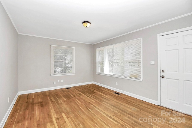 empty room with hardwood / wood-style floors and crown molding