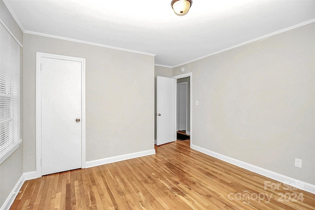 unfurnished bedroom featuring crown molding, light hardwood / wood-style floors, and a closet