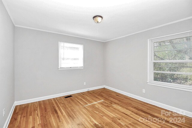 empty room featuring hardwood / wood-style flooring, plenty of natural light, and crown molding