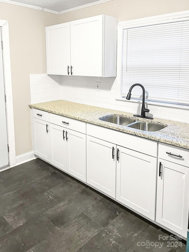 kitchen with light stone counters, white cabinets, ornamental molding, sink, and tasteful backsplash