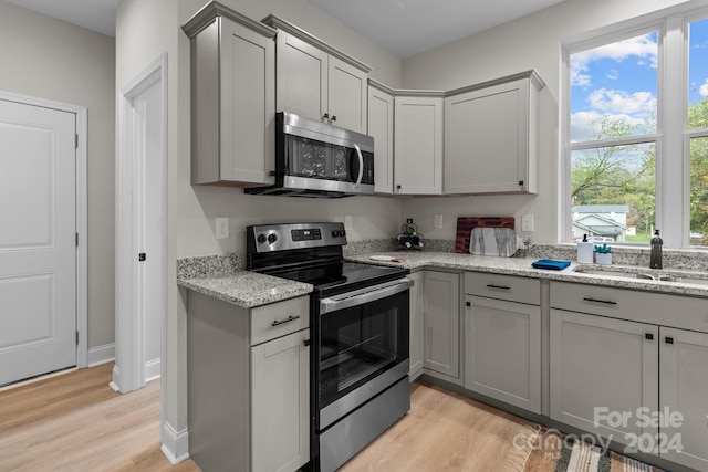 kitchen featuring light wood-type flooring, stainless steel appliances, light stone counters, and gray cabinetry