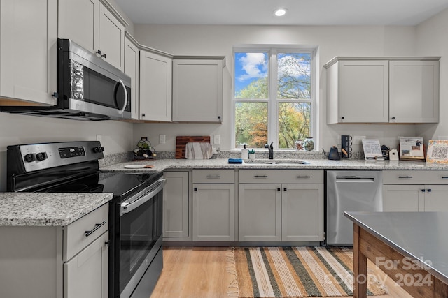 kitchen featuring sink, appliances with stainless steel finishes, light stone countertops, light hardwood / wood-style flooring, and gray cabinetry