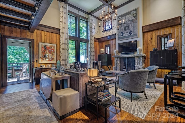 living room with beam ceiling, dark hardwood / wood-style flooring, a towering ceiling, a stone fireplace, and a chandelier