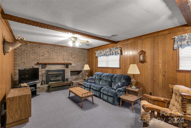 carpeted living room featuring brick wall, a brick fireplace, ceiling fan, beamed ceiling, and a textured ceiling