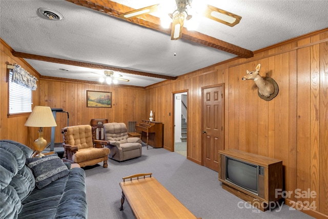 living room with ceiling fan, wooden walls, light colored carpet, and beamed ceiling