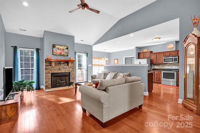 living room featuring lofted ceiling, a wealth of natural light, a stone fireplace, and light hardwood / wood-style floors