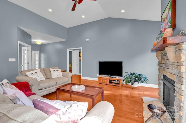 living room with ceiling fan, a stone fireplace, lofted ceiling, and light wood-type flooring