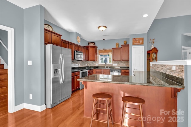 kitchen featuring sink, appliances with stainless steel finishes, a kitchen bar, decorative backsplash, and kitchen peninsula