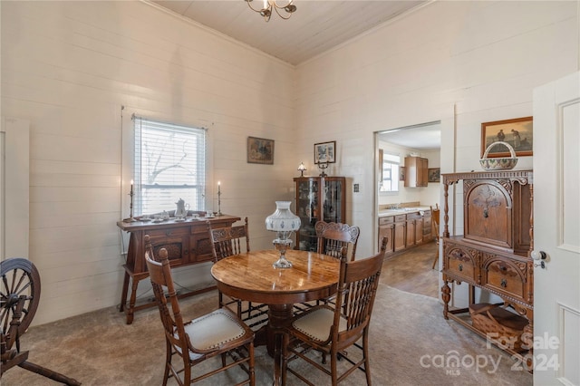 carpeted dining space with wood walls, a chandelier, and a healthy amount of sunlight