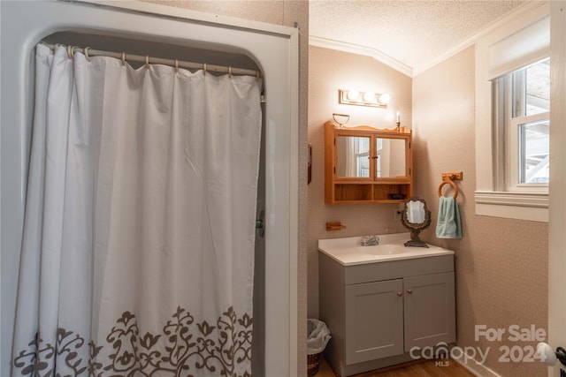 bathroom featuring ornamental molding, wood-type flooring, vaulted ceiling, oversized vanity, and a textured ceiling