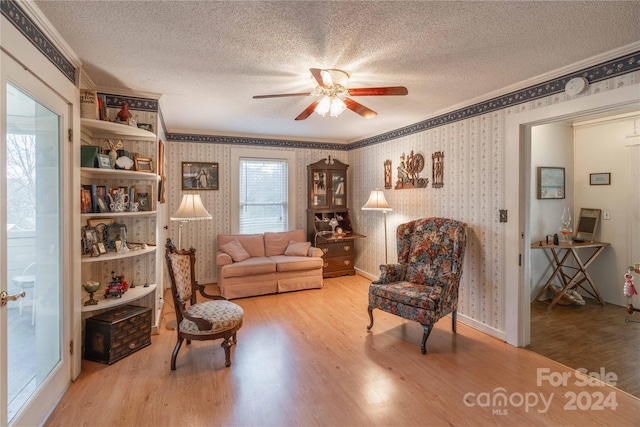 living room featuring ceiling fan, a textured ceiling, light hardwood / wood-style floors, and crown molding