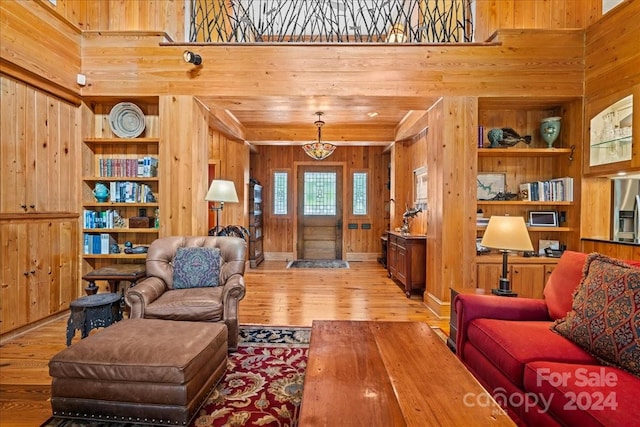 living room featuring a towering ceiling, built in features, wood walls, and light hardwood / wood-style flooring