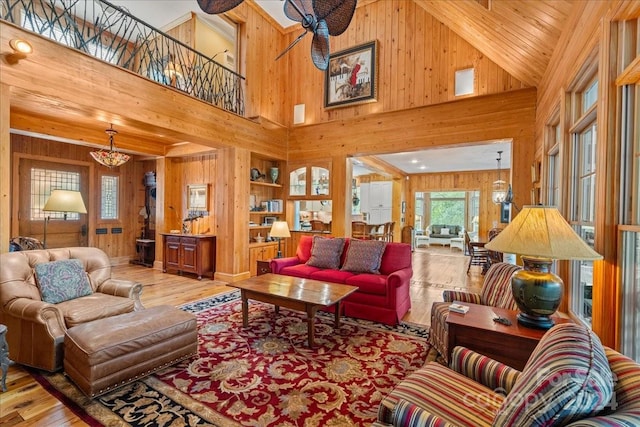 living room with high vaulted ceiling, wood walls, a chandelier, and light hardwood / wood-style floors