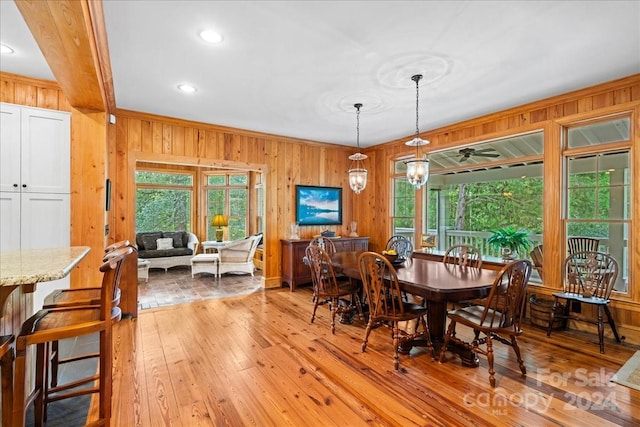 dining space with ceiling fan with notable chandelier, wood walls, and light hardwood / wood-style flooring