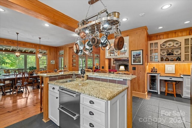 kitchen featuring a brick fireplace, beverage cooler, sink, a center island with sink, and white cabinets