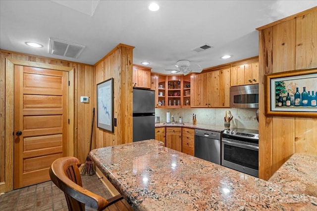 kitchen with appliances with stainless steel finishes, light stone counters, ceiling fan, a kitchen bar, and sink