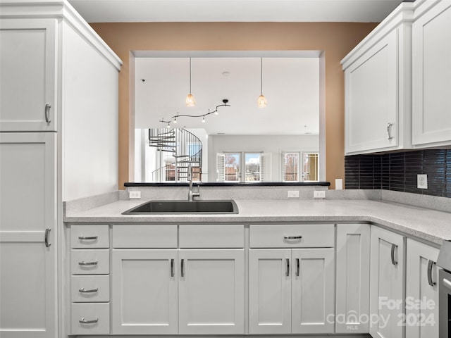 kitchen with sink, light stone counters, white cabinets, tasteful backsplash, and decorative light fixtures