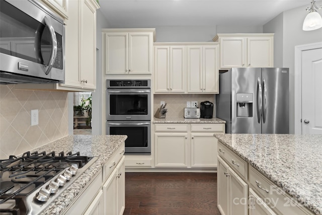 kitchen featuring backsplash, light stone countertops, stainless steel appliances, and cream cabinets