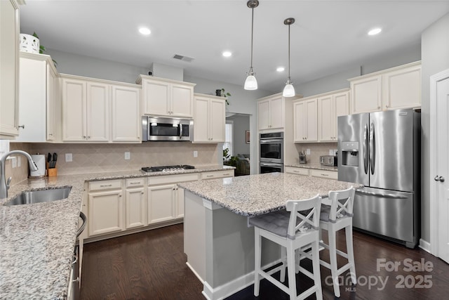 kitchen featuring light stone countertops, sink, a center island, decorative backsplash, and appliances with stainless steel finishes