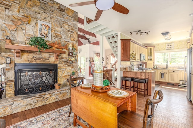 dining space with ceiling fan, sink, wood-type flooring, and a stone fireplace