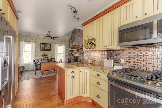 kitchen with kitchen peninsula, ceiling fan, appliances with stainless steel finishes, backsplash, and light hardwood / wood-style flooring