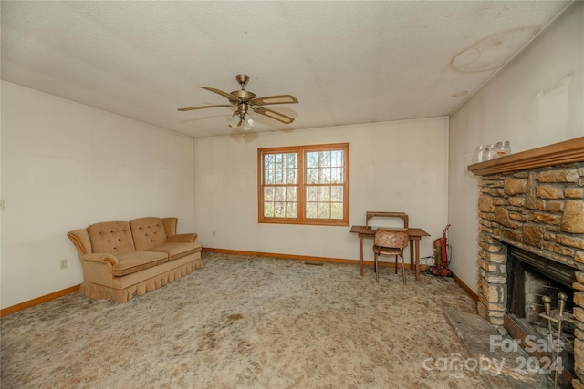 living area featuring ceiling fan, a textured ceiling, carpet floors, and a stone fireplace