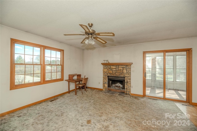 unfurnished living room featuring ceiling fan, a textured ceiling, and a stone fireplace