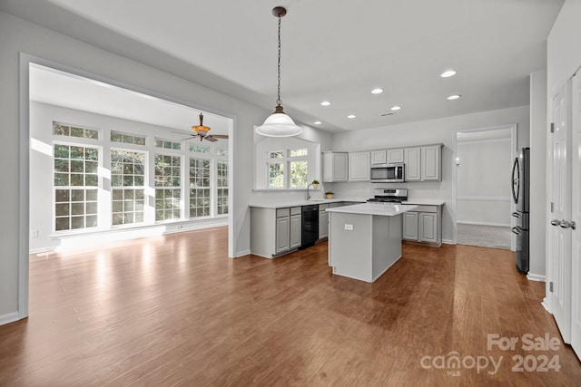 kitchen with appliances with stainless steel finishes, hanging light fixtures, light hardwood / wood-style floors, a kitchen island, and gray cabinets