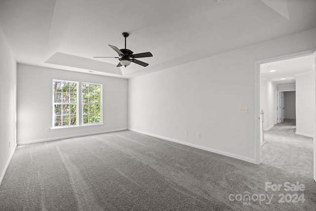 empty room with light carpet, a tray ceiling, and ceiling fan