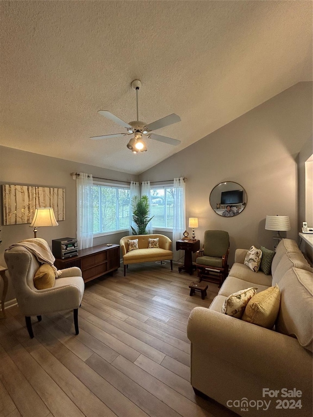 living room featuring ceiling fan, lofted ceiling, light hardwood / wood-style flooring, and a textured ceiling