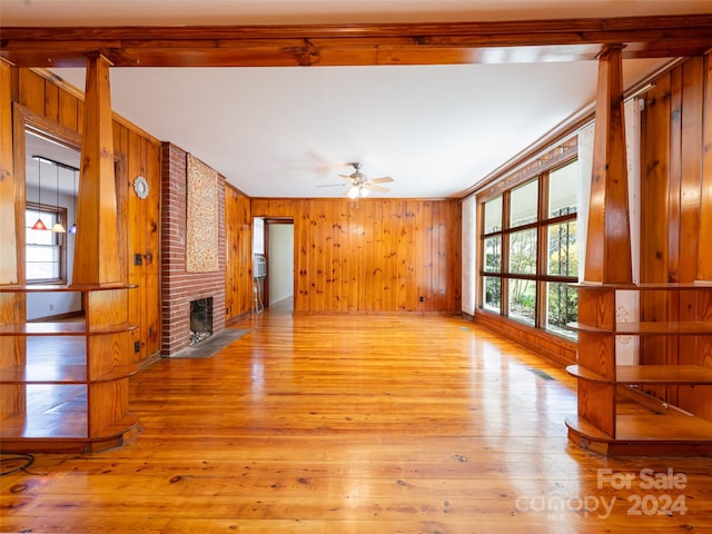 empty room with wooden walls, ceiling fan, a fireplace, and light hardwood / wood-style floors