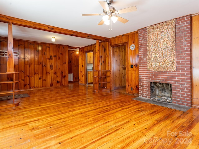 unfurnished living room with light hardwood / wood-style flooring, brick wall, a fireplace, and wooden walls