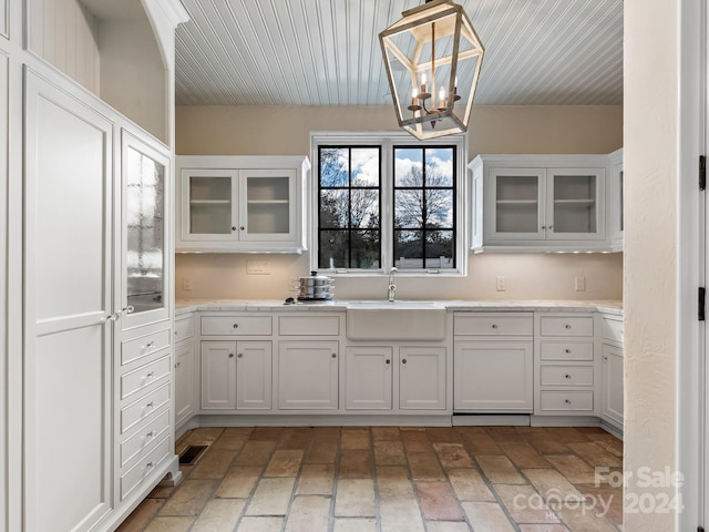 kitchen featuring white cabinets, hanging light fixtures, a chandelier, and sink