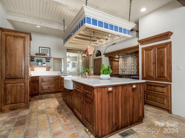 kitchen featuring decorative light fixtures, a center island with sink, sink, and beamed ceiling