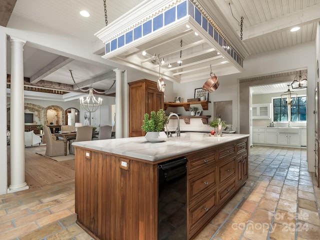 kitchen featuring a kitchen island with sink, decorative columns, a chandelier, and light stone countertops