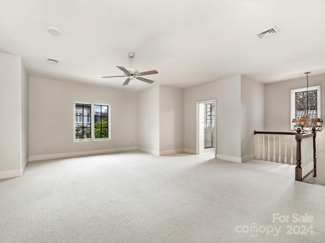 carpeted empty room featuring ceiling fan with notable chandelier