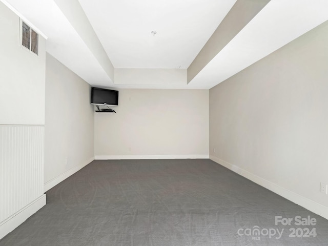 empty room with dark colored carpet and a tray ceiling