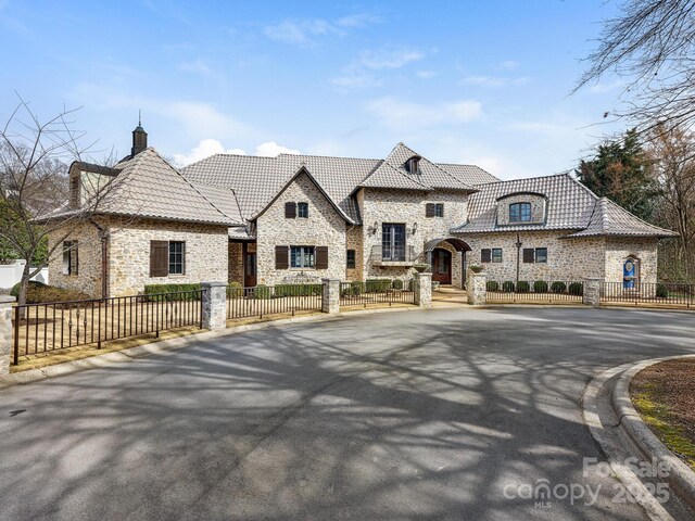 french country style house featuring stone siding, a fenced front yard, and a tiled roof