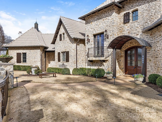 rear view of house featuring stone siding, french doors, a tile roof, and a chimney