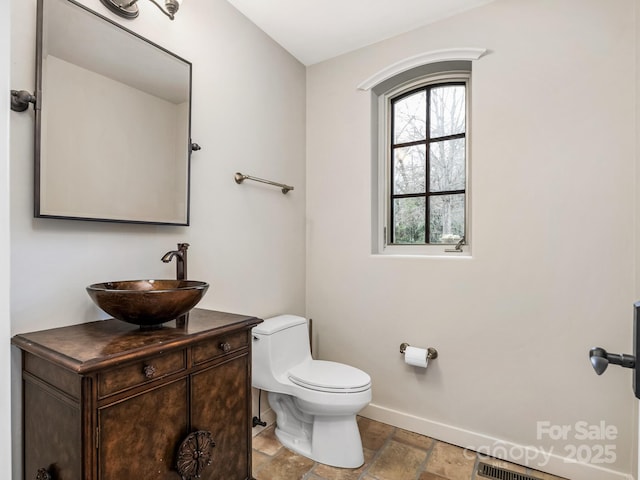 bathroom featuring toilet, stone finish flooring, baseboards, and vanity