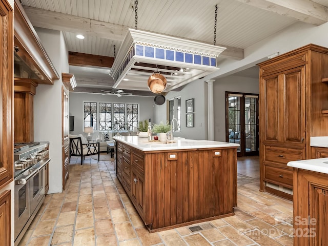 kitchen with range with two ovens, light countertops, a kitchen island with sink, and beamed ceiling