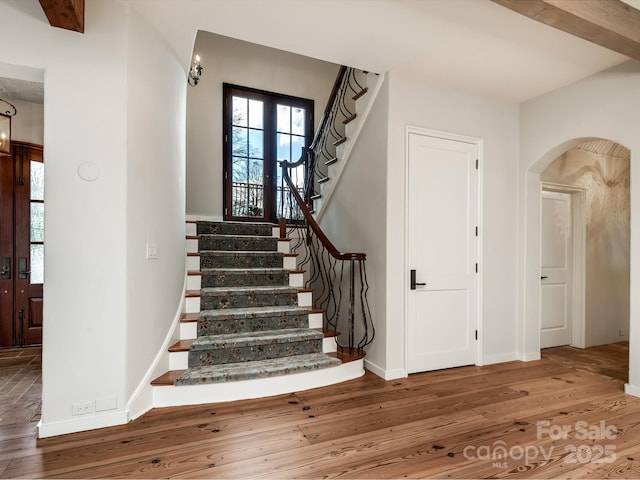 stairs with baseboards, arched walkways, wood finished floors, and french doors