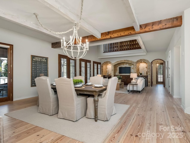 dining area featuring arched walkways, a notable chandelier, baseboards, light wood finished floors, and beamed ceiling