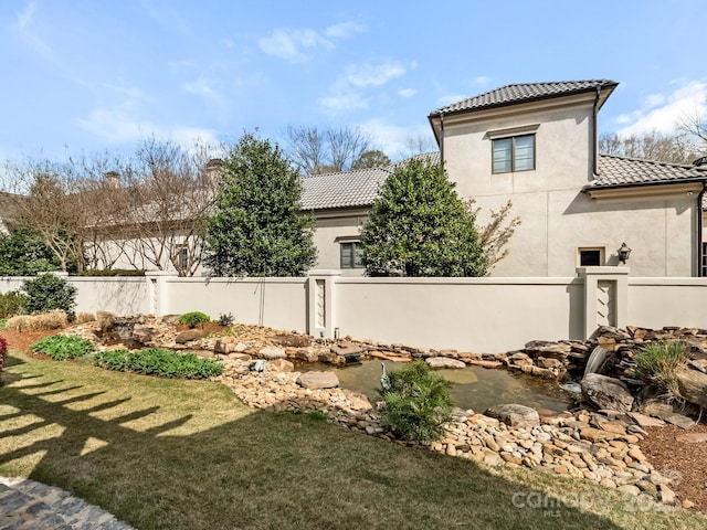 view of home's exterior with fence private yard, a tile roof, a yard, and stucco siding