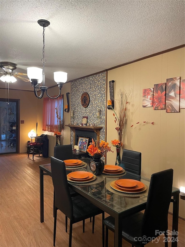 dining area with a fireplace, light hardwood / wood-style floors, a textured ceiling, and ceiling fan with notable chandelier