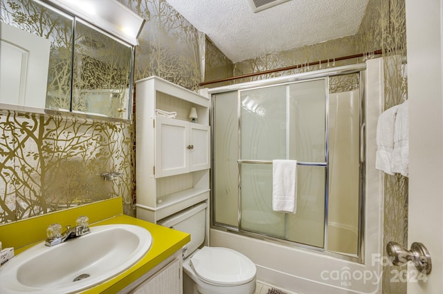 full bathroom with a textured ceiling, combined bath / shower with glass door, toilet, and vanity