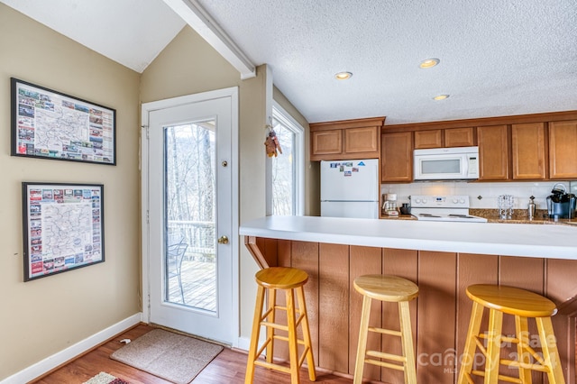 kitchen with a breakfast bar, white appliances, light wood-type flooring, and vaulted ceiling