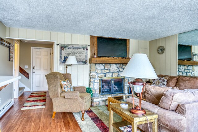 living room featuring wooden walls, a textured ceiling, wood-type flooring, and a stone fireplace