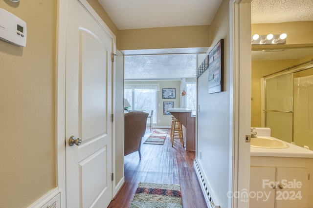 hall featuring a baseboard heating unit, a textured ceiling, dark hardwood / wood-style floors, and sink